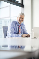 Businessman sitting at desk using laptop - RBF002684