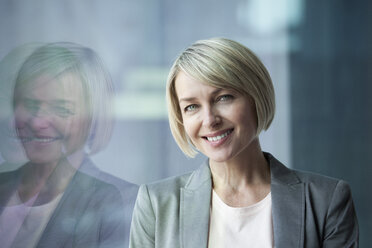 Businesswoman standing at window, smiling, portrait - RBF002689