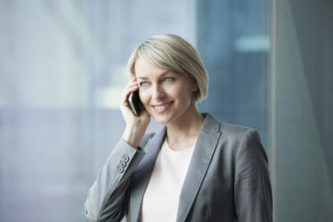 Geschäftsfrau steht am Fenster und benutzt ein Mobiltelefon - RBF002690