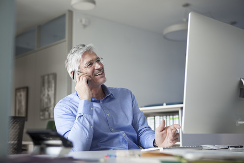 Businessman sitting at desk, talking on the phone stock photo