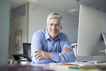 Businessman sitting at desk, arms crossed, looking content - RBF002737