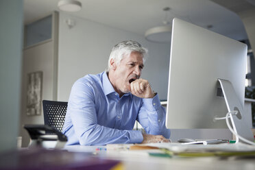 Businessman sitting at desk, yawning - RBF002739