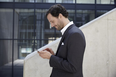 Businessman using smartphone in a modern building - FMKF001521