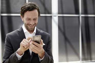 Businessman using smartphone in a modern building - FMKF001524