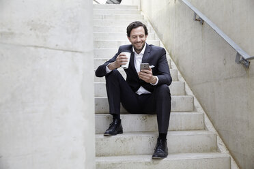 Geschäftsmann mit Kaffee zum Mitnehmen und Smartphone in einem modernen Gebäude - FMKF001526