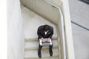 Businessman sitting on stairs of a modern building using laptop - FMKF001535