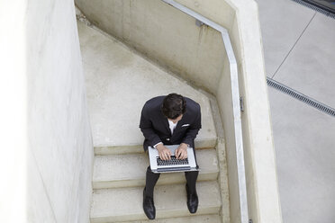 Geschäftsmann sitzt auf der Treppe eines modernen Gebäudes und benutzt einen Laptop - FMKF001535