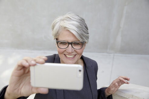 Porträt einer lächelnden Karrierefrau, die ein Selfie mit ihrem Smartphone macht - FMKF001544