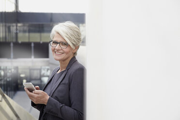 Portrait of smiling businesswoman with smartphone - FMKF001562