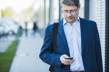 Germany, Portrait of a mature businessman in street holding smart phone - UUF004080