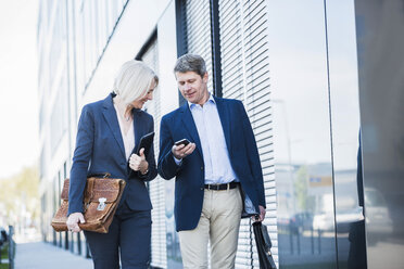 Businesspeople walking in street checking smart phone - UUF004086