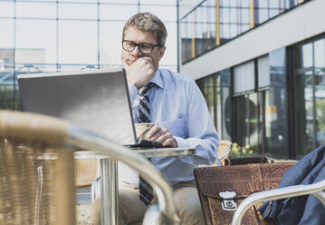 Germany, Businessman sitting in cafeteria working at laptop - UUF004103