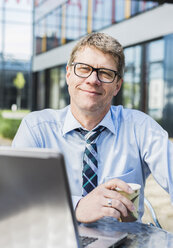 Germany, Businessman sitting in cafeteria working at laptop - UUF004107