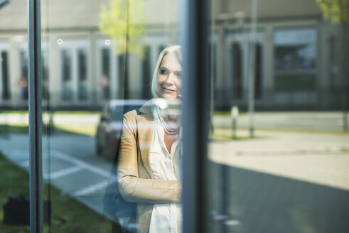 Reife Frau betrachtet ihr gespiegeltes Selbst an der Fensterscheibe - UUF004119