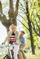 Mature couple riding bike in park, man sitting on rack - UUF004121