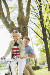 Mature couple riding bike in park, man sitting on rack - UUF004122