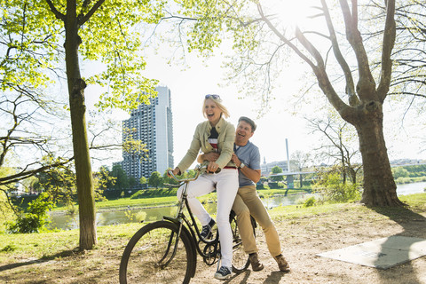 Älteres Paar fährt Fahrrad im Park, Mann sitzt auf dem Gepäckträger, lizenzfreies Stockfoto