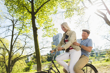 Älteres Paar fährt Fahrrad im Park, Mann sitzt auf dem Gepäckträger - UUF004124