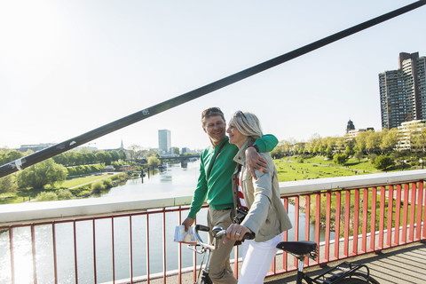 Deutschland, Mannheim, Älteres Paar überquert Brücke, schiebt Fahrrad, lizenzfreies Stockfoto