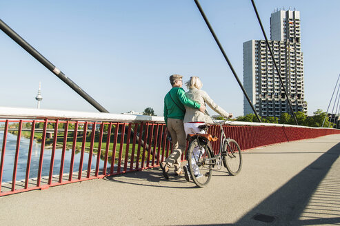 Deutschland, Mannheim, Älteres Paar überquert Brücke, schiebt Fahrrad - UUF004143