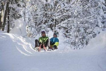 Germany, Bavaria, Inzell, couple having fun on sledges in snow-covered landscape - FFF001439