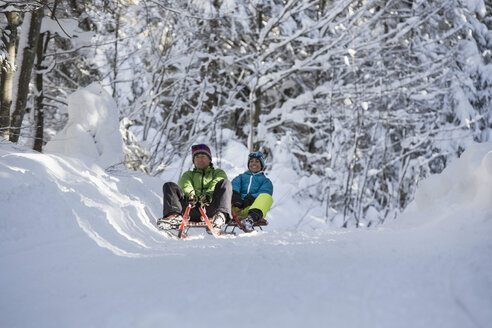 Germany, Bavaria, Inzell, couple having fun on sledges in snow-covered landscape - FFF001439