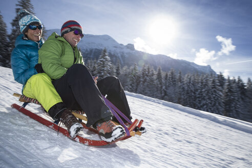 Germany, Bavaria, Inzell, couple having fun on a sledge in snow-covered landscape - FFF001440