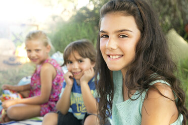 Portrait of smiling girl outdoors with siblings in background - TOYF000244