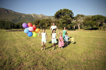 Glückliche Familie mit Luftballons auf der Wiese - TOYF000264