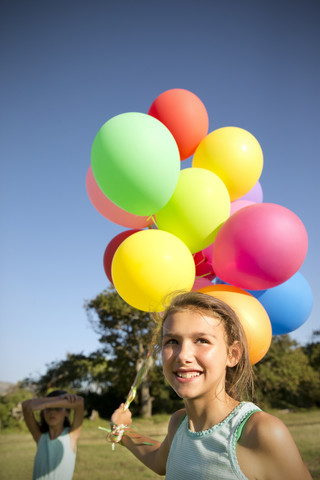 Lächelndes Mädchen hält ein Bündel Luftballons im Freien, lizenzfreies Stockfoto