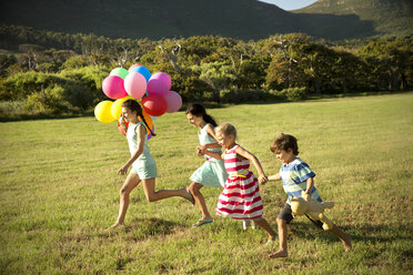 Fröhliche Kinder laufen mit Luftballons auf einer Wiese - TOYF000266