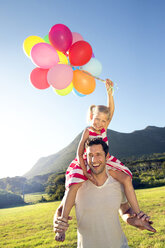 Happy father carrying daughter with balloons on shoulders - TOYF000268