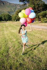 Happy girl running with balloons on meadow - TOYF000269