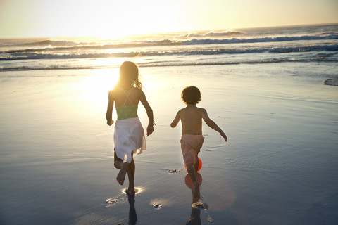 Junge und Mädchen laufen am Strand bei Sonnenuntergang, lizenzfreies Stockfoto