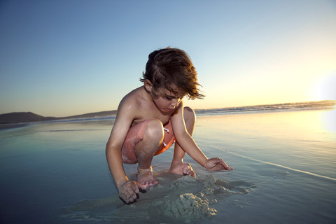 Junge spielt am Strand bei Sonnenuntergang, lizenzfreies Stockfoto