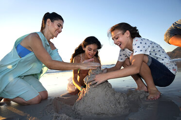 Mutter und zwei Töchter bauen eine Sandburg am Strand - TOYF000295