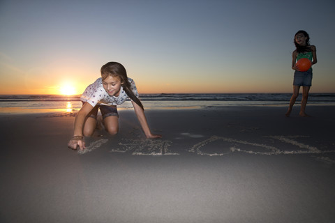 Mädchen am Strand bei Sonnenuntergang Zeichnung in Sand, lizenzfreies Stockfoto