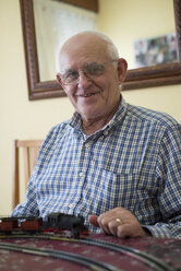 Porträt eines lächelnden älteren Mannes mit seiner Modelleisenbahn - RAEF000177