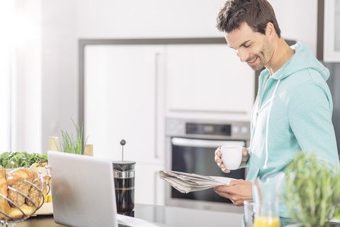 Mann mit einer Tasse Kaffee, der in der Küche Zeitung liest, lizenzfreies Stockfoto