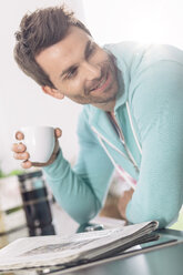 Porträt eines Mannes mit einer Tasse Kaffee und einer Zeitung in der Küche - MADF000237