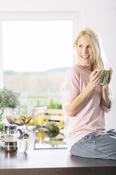Porträt einer lächelnden jungen Frau mit einer Tasse Kaffee in der Küche - MADF000277