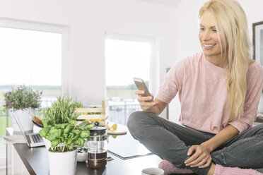 Smiling young woman with smartphone in the kitchen - MADF000279