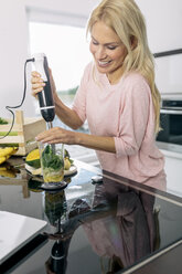 Lächelnde junge Frau bei der Zubereitung eines Smoothies in der Küche - MADF000283