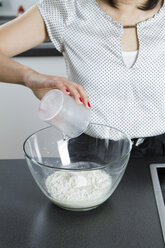 Frau gießt Wasser in eine Glasschüssel mit Mehl - FLF001041