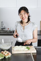 Porträt einer lächelnden Frau beim Schneiden von Frühlingszwiebeln in einer Küche - FLF001044