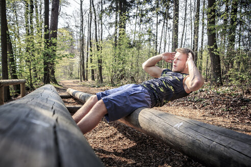 Deutschland, Coburg, Junger Mann übt Sit-ups auf einem Fitnessparcours im Wald - VTF000420