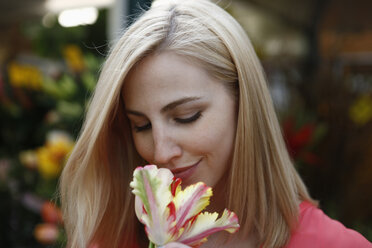Blonde Frau riecht an einer Blume auf dem Wochenmarkt - RHF000820