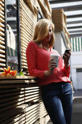 Lächelnde blonde Frau mit Coffee to go und Smartphone - RHF000826