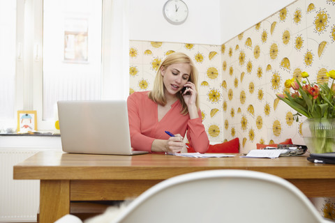 Junge Frau telefoniert mit Smartphone in ihrem Büro zu Hause, lizenzfreies Stockfoto