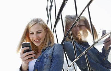 Germany, Duesseldorf, portrait of smiling blond woman looking at smartphone - RHF000853